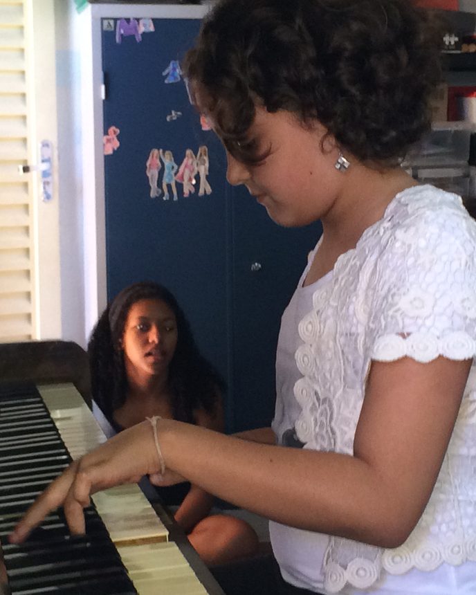 Aluna ao piano em aula na TaCaTum, com a professora acompanhando