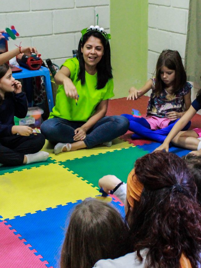 Turma de musicalização sentada no tatame colorido com a professora